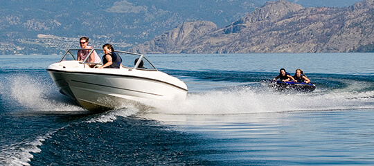 A boat on a lake pulling along people on a tube.