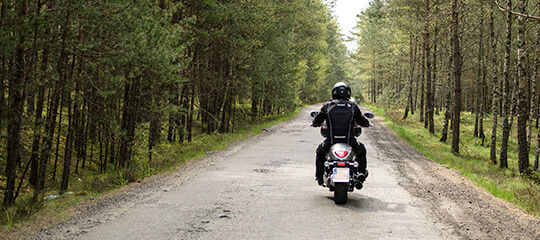 A motorcycle going down a road in the woods.